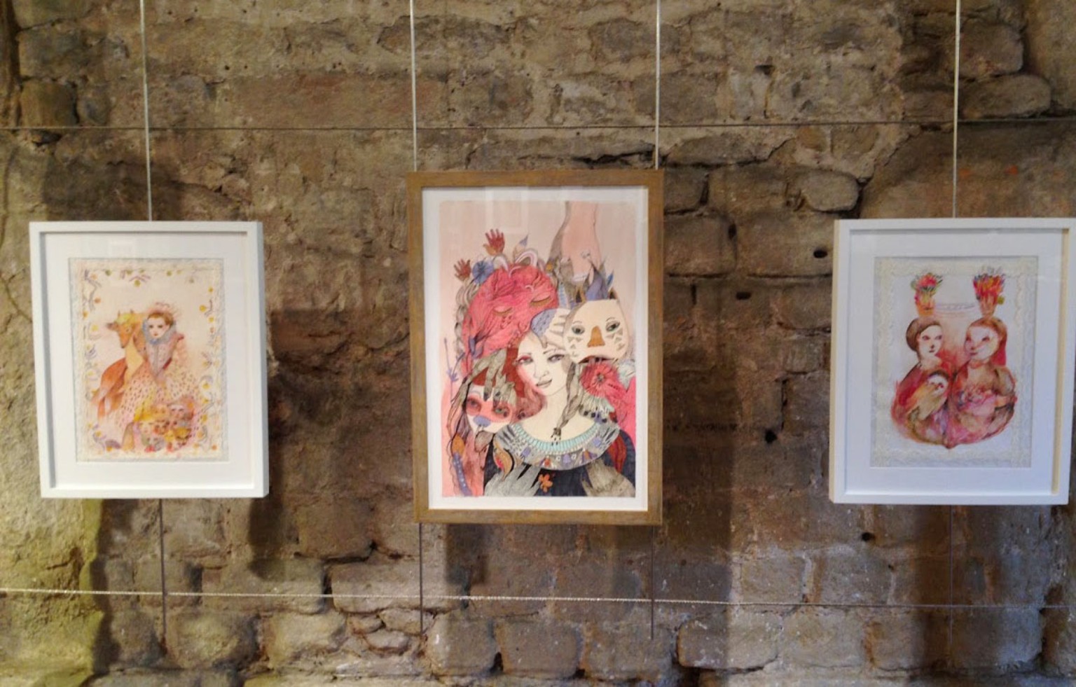 Three framed works featuring figures and animals on a stone wall.