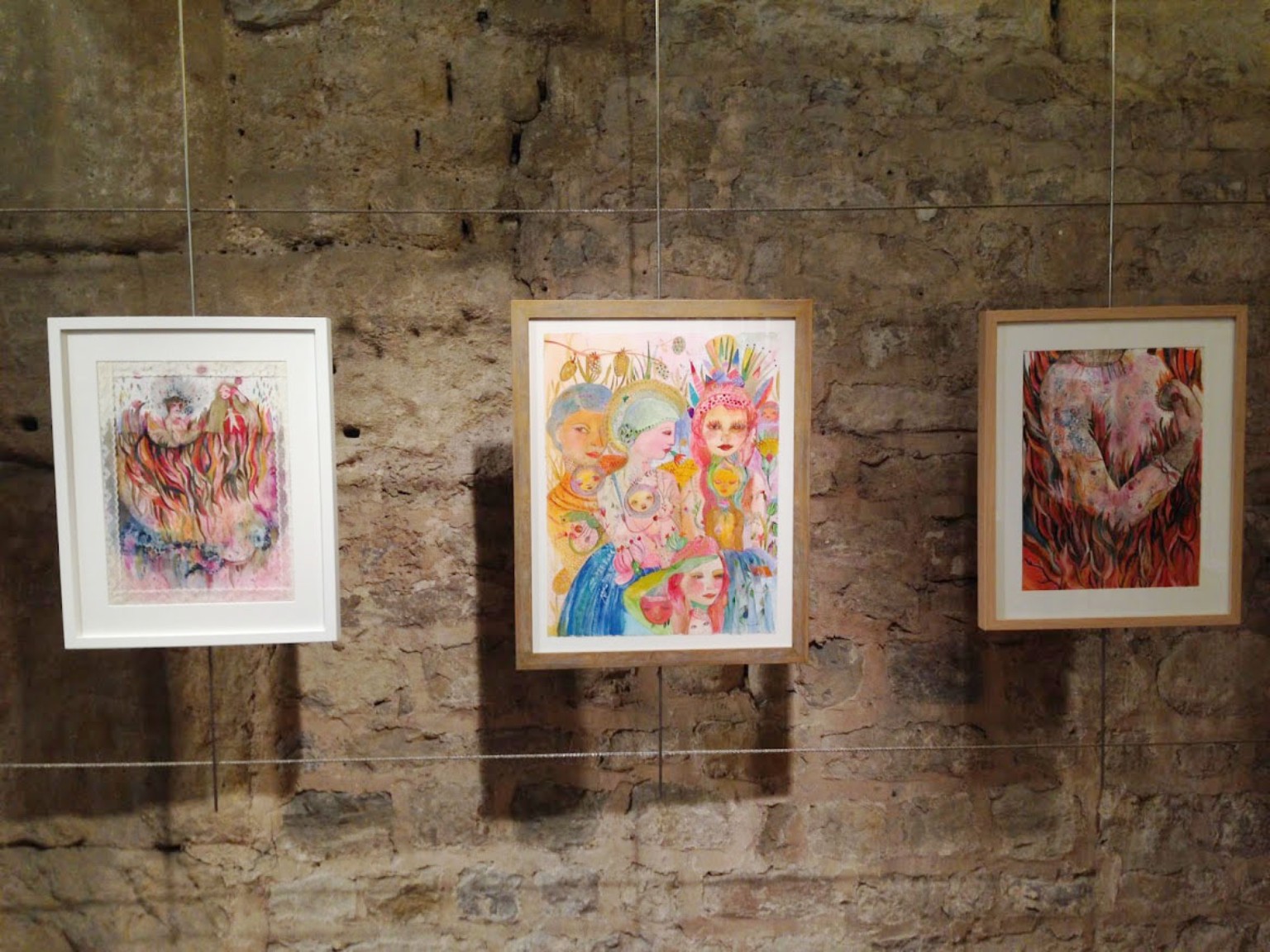 Three framed paintings of female figures hanging on a stone wall.